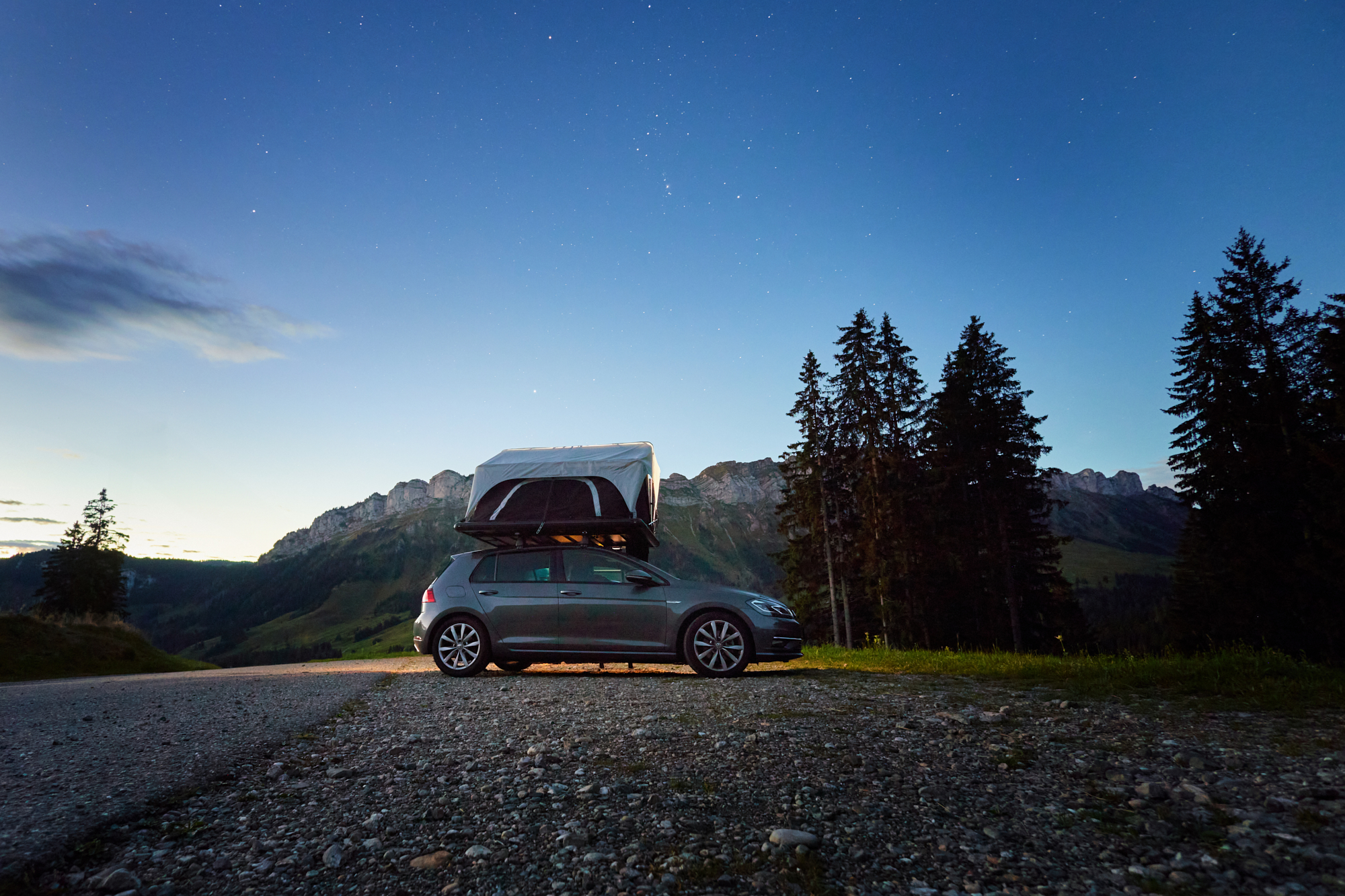 VW Golf mit aufgeklapptem Dachzelt mit Bergen im Hintergrund unter Sternenhimmel, aufgenommen in Entlebuch in der Schweiz